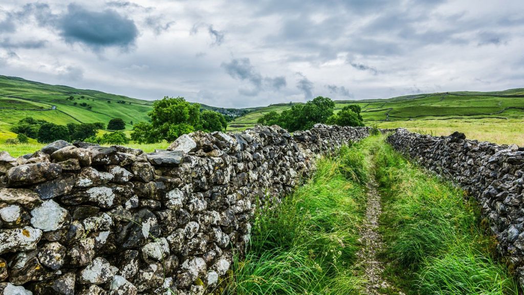 View of farmland stretching into the distance taken from a walking path between two ancient stone walls