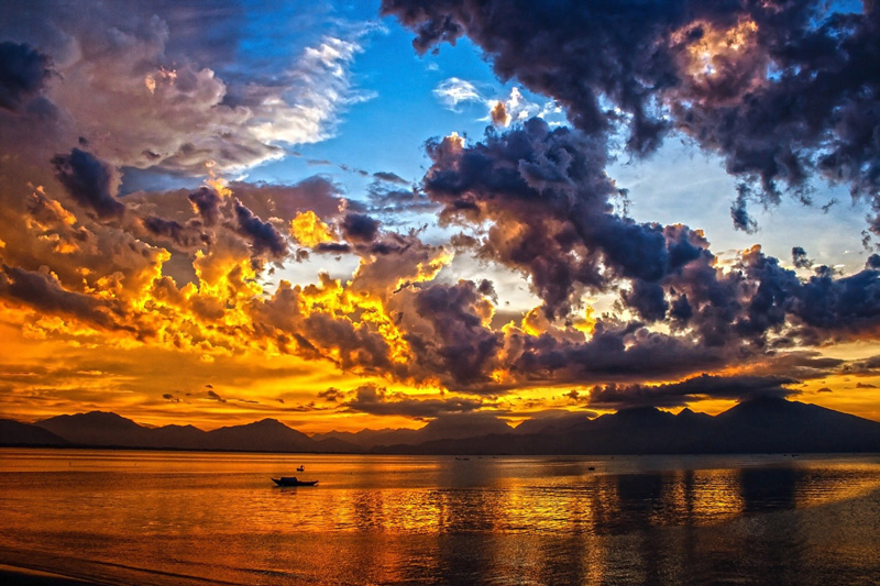 Beautiful sunset of mixed light and clouds, reflected off water in the foreground with majestic mountains in the distance