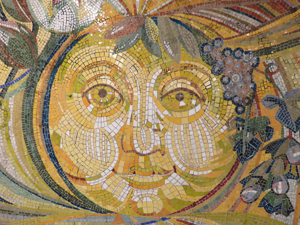 Mosaic artwork featuring bright sun with human face with grape leaves and vines